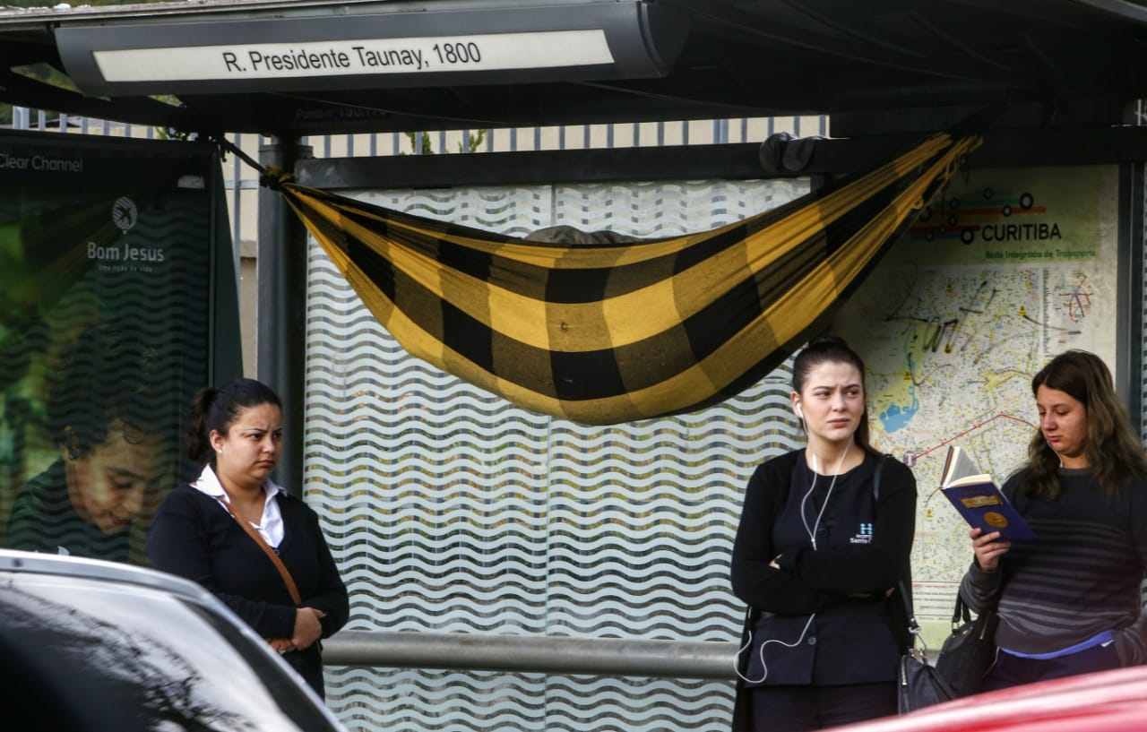 O homem amarra sua rede na parte superior do ponto de ônibus e a enche de papelão para que fique mais quente | Aniele Nascimento/Gazeta do Povo