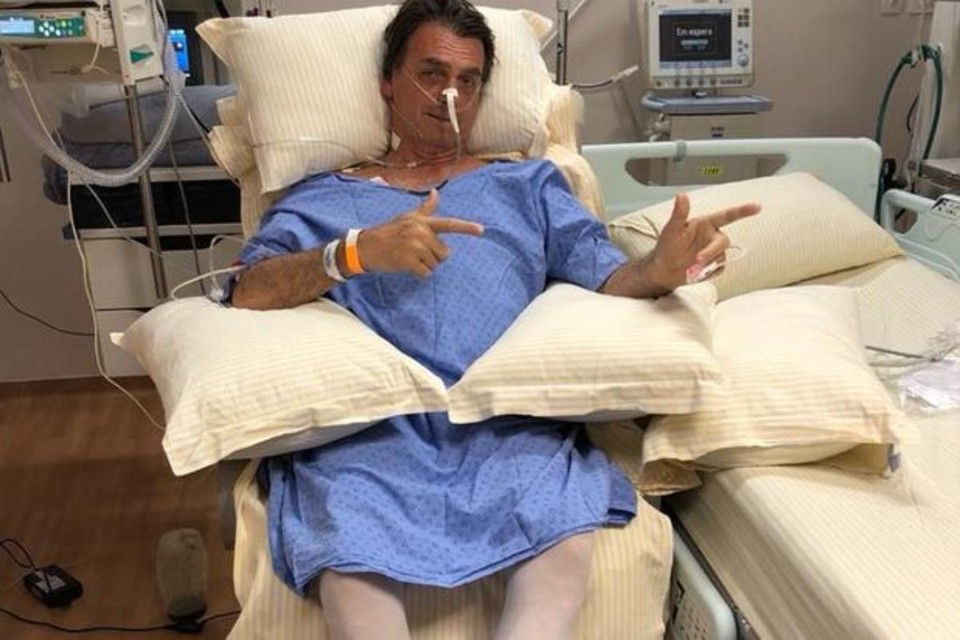 O candidato à presidência Jair Bolsonaro faz o sinal típico de sua campanha no hospital |