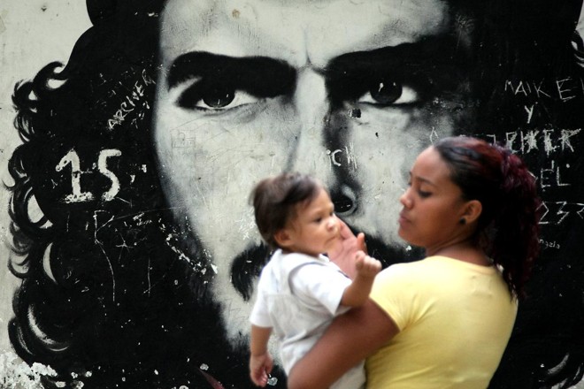 Uma mãe com seu filho passa por um grafitti retratando o revolucionário argentino Ernesto Che Guevara em um bairro de baixa renda de Caracas, em 8 de outubro de 2008. | THOMAS COEX/AFP