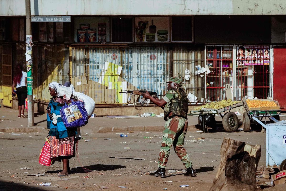 Um vendedor tenta se esconder com seus produtos enquanto soldados dispersam manifestantes que protestaram contra a eleição de Emmerson Mnangagwa, em 1º de agosto de 2018, em Harare | ZINYANGE AUNTONY/
AFP