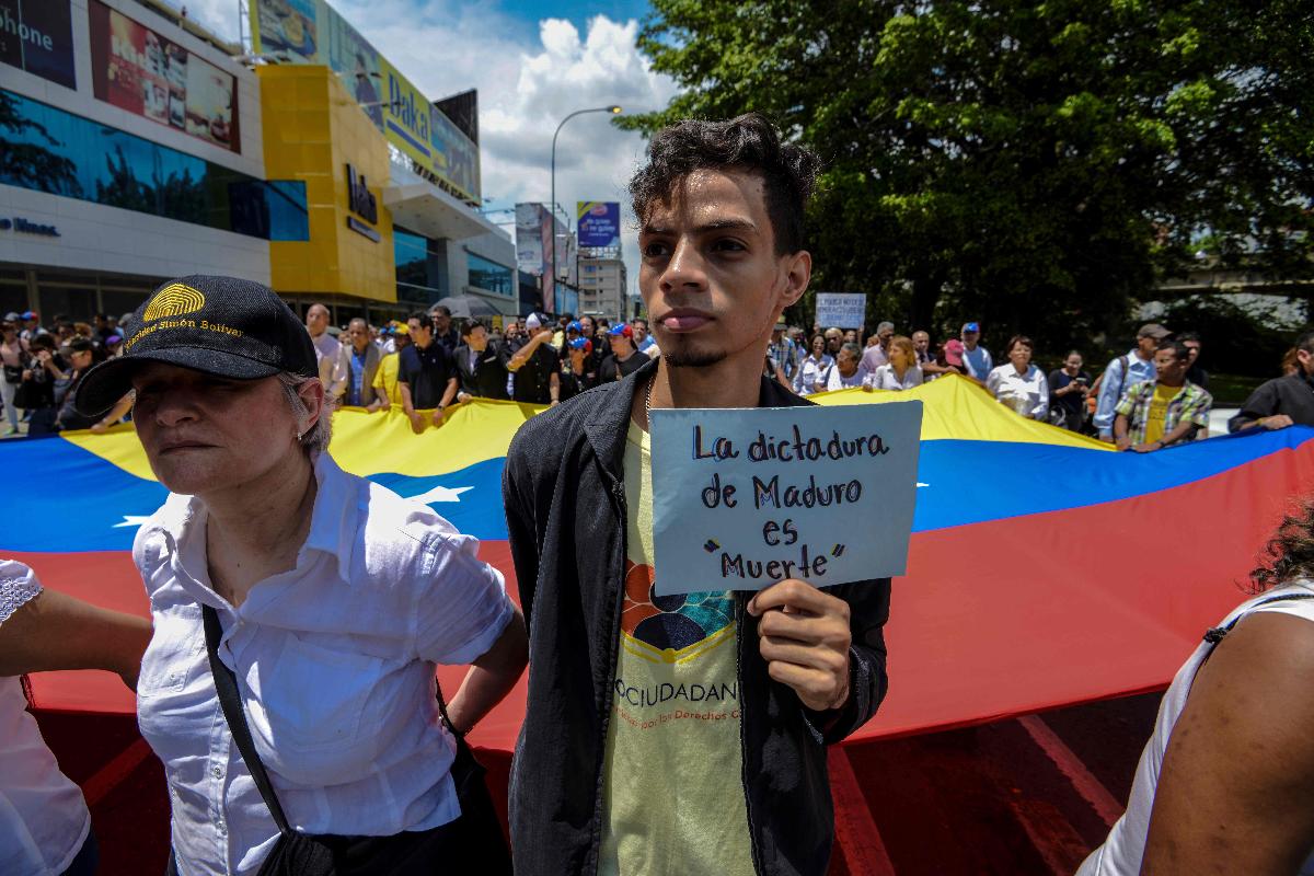 Pessoas carregam uma enorme bandeira venezuelana durante o cortejo fúnebre do falecido vereador da oposição Fernando Alban | JUAN BARRETO/AFP