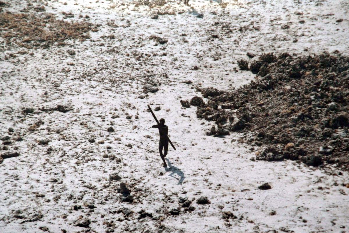 Foto de dezembro de 2004 mostra um homem da tribo Sentineleses apontando seu arco e flecha para um helicóptero da Guarda Costeira Indiana, após o grande tsunami que atingiu a região | AFP