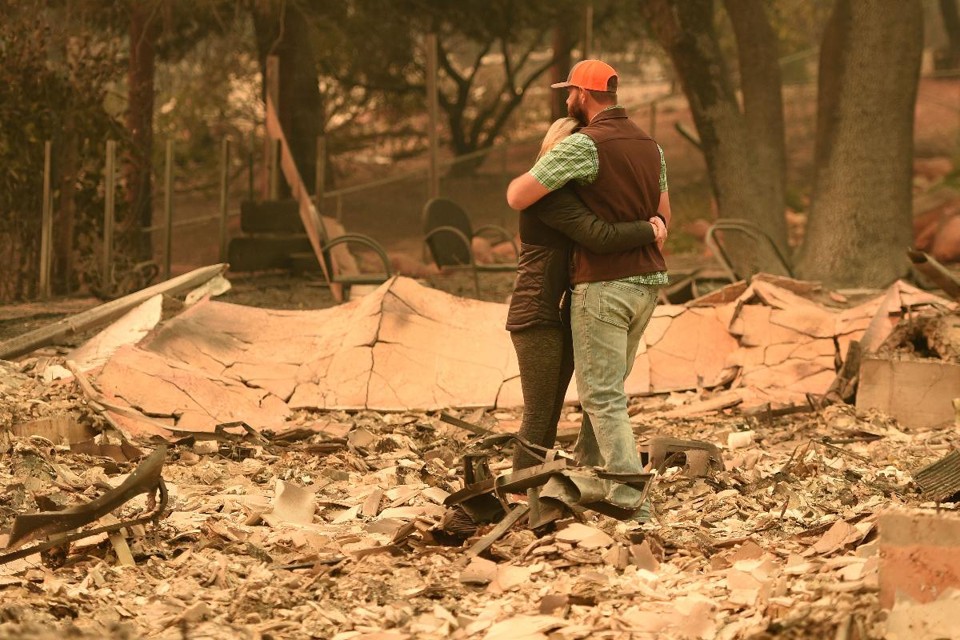 Um casal se abraça enquanto examina os escombros de sua residência após o incêndio Camp Fire ter atingido a cidade de Paradise, na Califórnia | JOSH EDELSON/AFP
