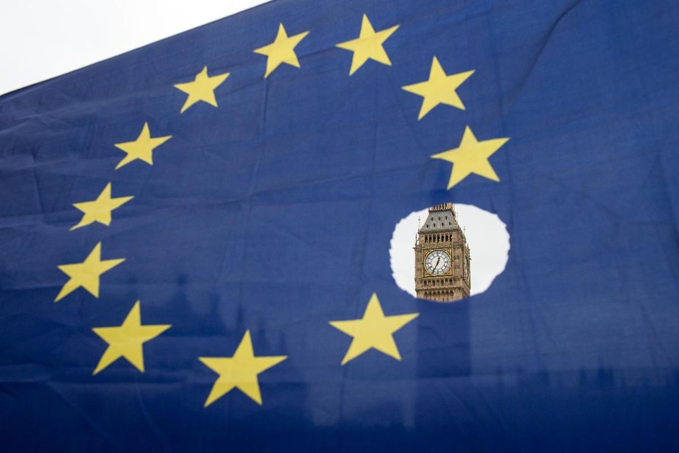 Bandeira da UE com uma das estrelas simbolicamente cortada, onde aparece, ao fundo, a torre das Casas do Parlamento, na Inglaterra | OLI SCARFF/AFP