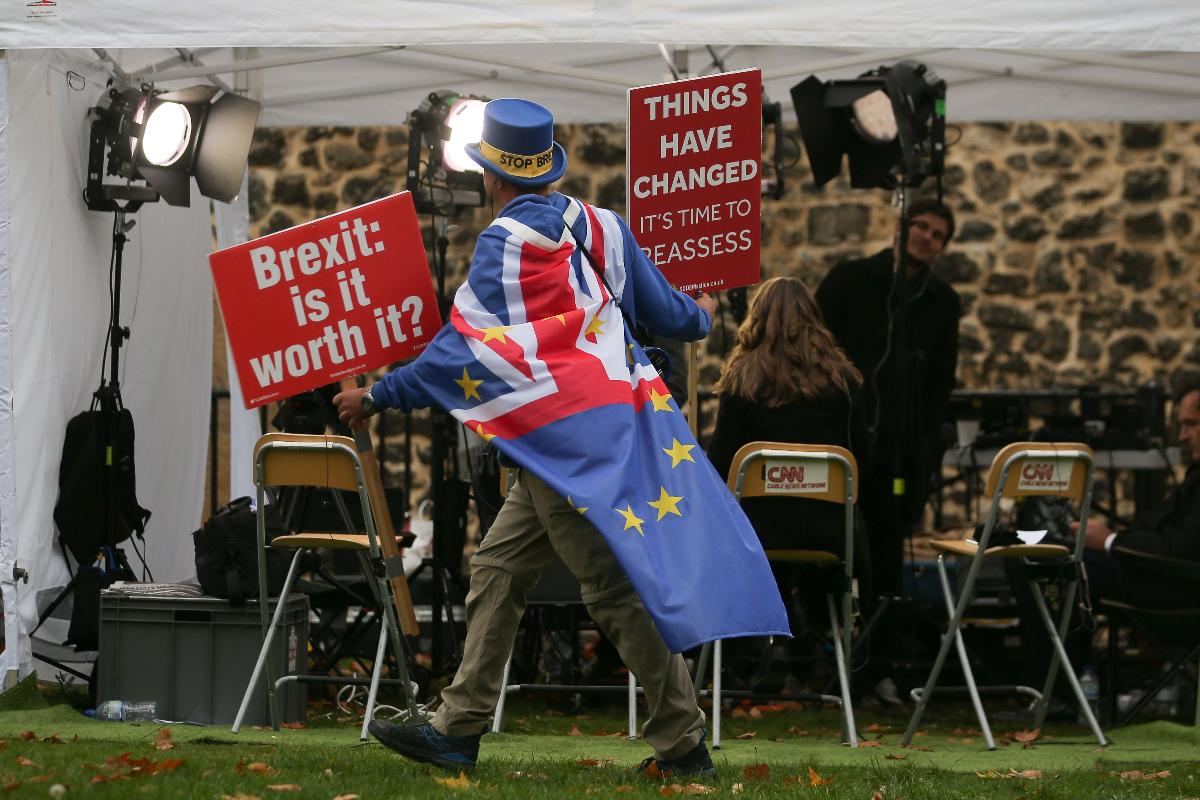 Manifestante com cartazes com slogans anti-Brexit passa por repórteres de TV perto do Parlamento em Londres, em 16 de novembro | DANIEL LEAL-OLIVAS / 
AFP