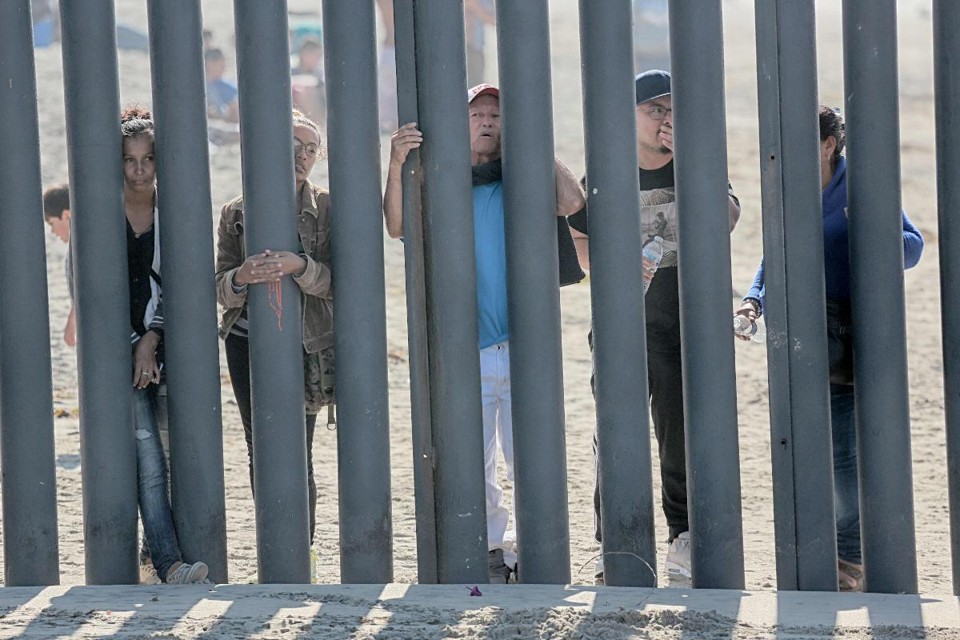 Nesta foto de arquivo tirada em 18 de novembro de 2018, imigrantes de Honduras olham pela cerca que delimita a fronteira EUA-México em San Ysidro, Califórnia | SANDY HUFFAKER/AFP