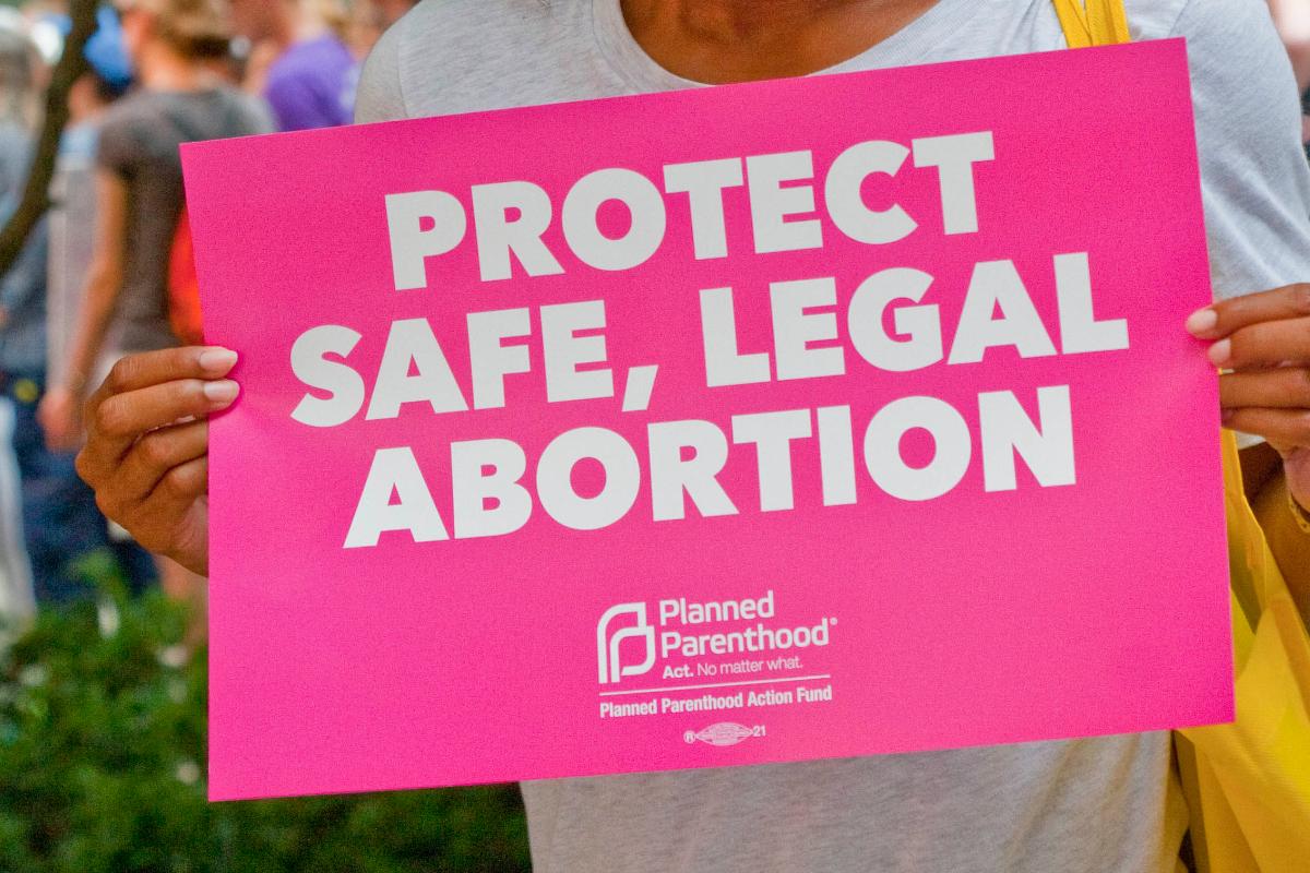 Durante manifestação promovida pela Planned Parenthood, mulher segura cartaz onde se lê “proteja o aborto seguro e legal”. | Charles Edward Miller/Flickr/Reprodução