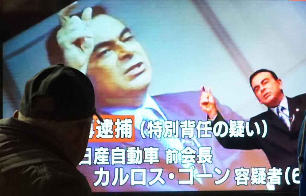 Pedestres olham imagens de Ghosn projetadas nos telões da cidade de Tóquio, no Japão. Executivo está preso no país desde 19 de novembro. | KAZUHIRO NOGI/AFP