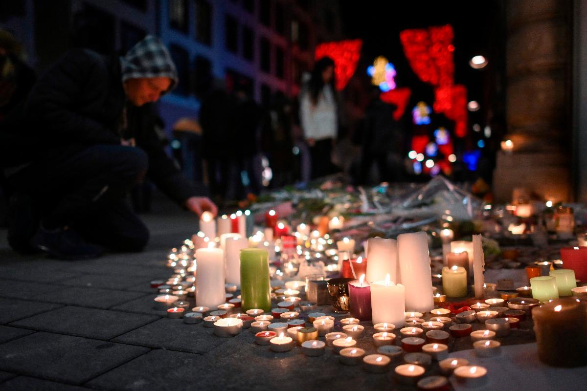 Pessoas acendem velas e deixam flores em homenagem às vítimas do tiroteio em Strasbourg, França. Três pessoas morreram e 13 ficaram feridas. | SEBASTIEN BOZON / AFP