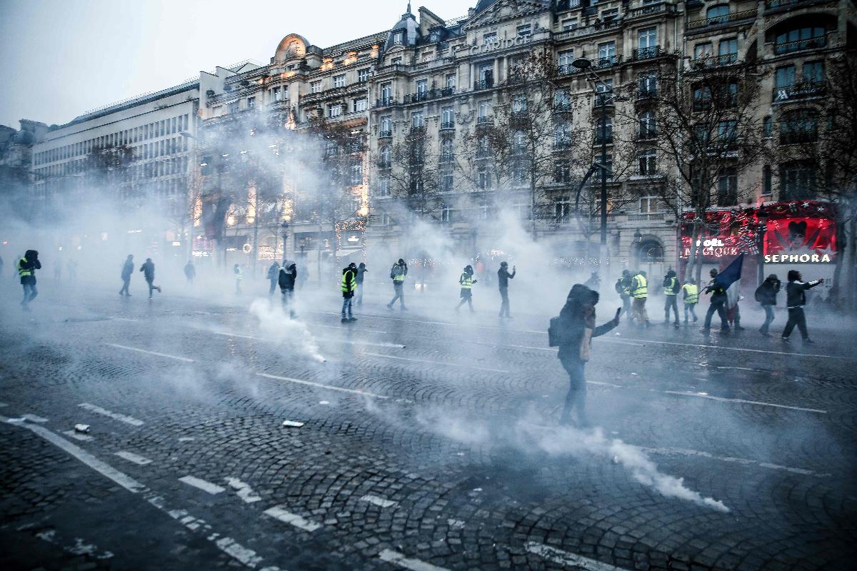 Manifestantes vestindo os coletes amarelos em meio ao gás lacrimogêneo durante protesto contra o alto custo de vida, na avenida Champs-Elysees, em Paris, 15 de dezembro | ABDUL ABEISSA / AFP