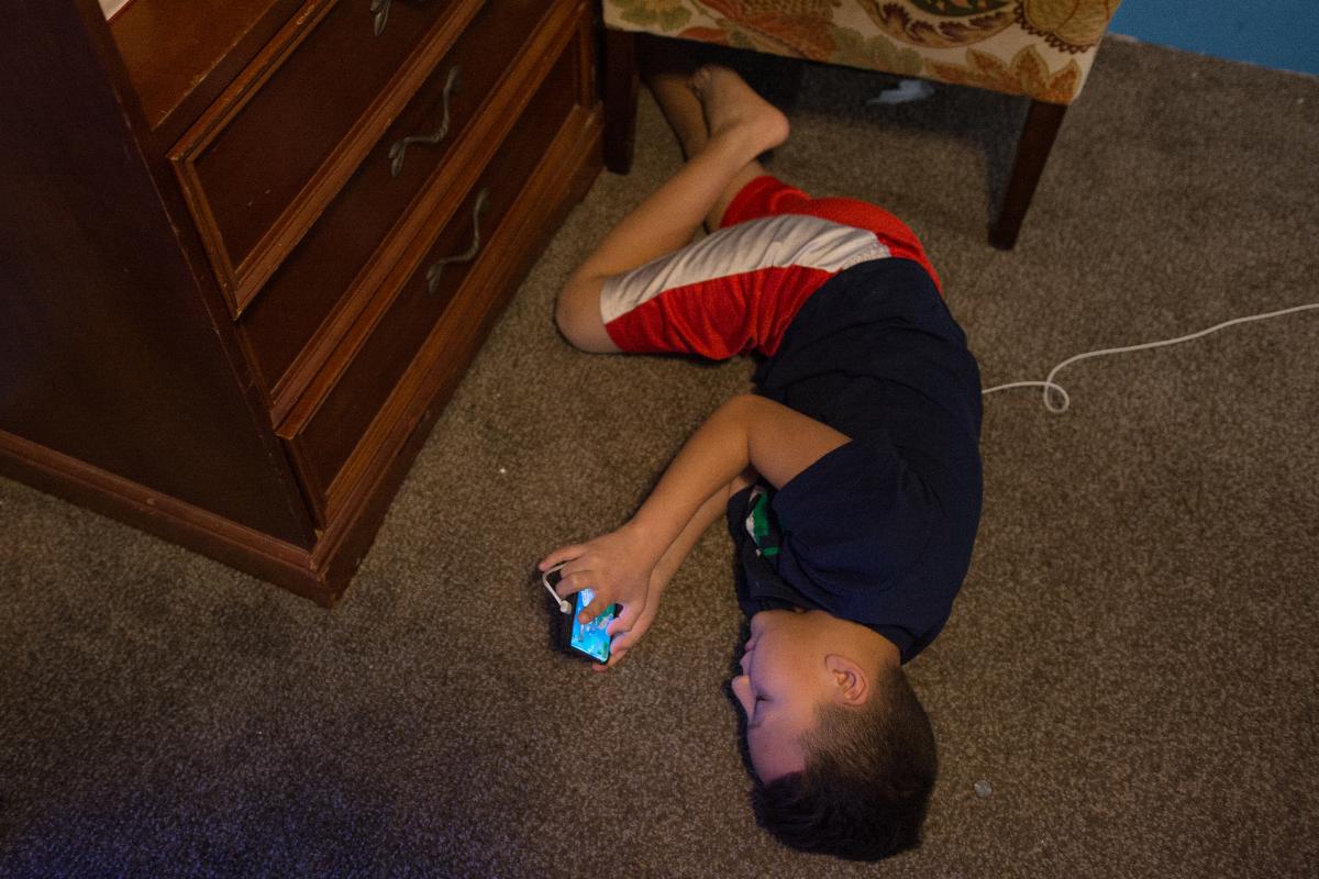 Isaac Flores Amador, 11, deitado no chão enquanto recebe uma ligação de sua mãe, que está a mais de 3.000 quilômetros de distância, em Honduras. | Sebastian Hidalgo/The Washington Post