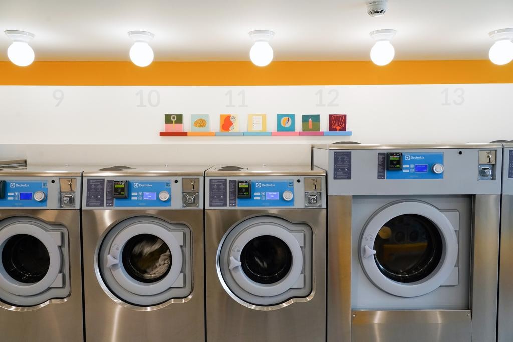 A lavandeira Celsious, no Brooklyn, em Nova York, abriga exposições de obras de arte ao fundo. Sim, obras de arte na lavanderia.