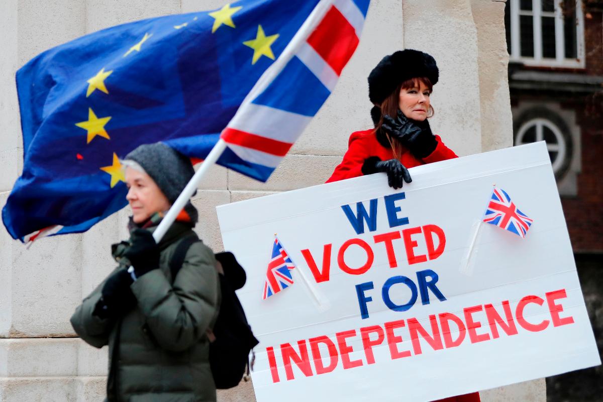 Manifestante pró-Brexit segura um cartaz que diz "Nós votamos por independência" ao lado de uma manifestante contra o Brexit que segura as bandeiras da União Europeia e do Reino Unido | TOLGA AKMEN / AFP