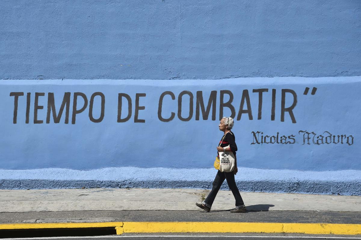 Mulher passa por um grafite em um muro onde se lê “Tempo de lutar”, atribuída ao ditador Nicolas Maduro, em Caracas, em 22 de janeiro de 2019 | YURI CORTEZ/AFP