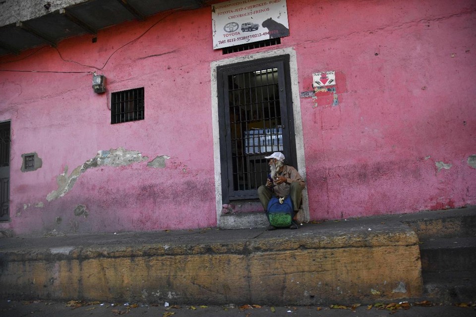Morador sentado na porta de uma casa no bairro de Cotiza, em Caracas | YURI CORTEZ/AFP