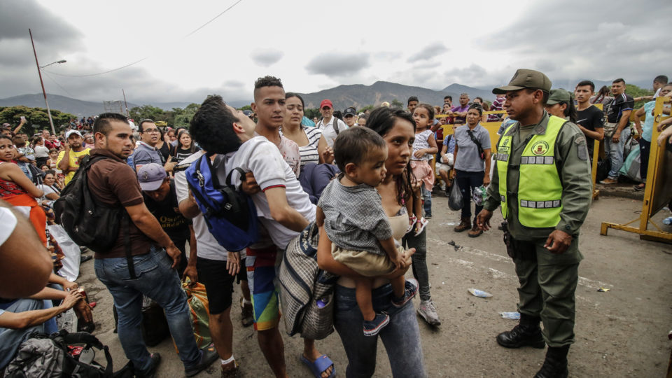 Homem leva no colo um estudante que desmaiou ao atravessar a ponte internacional Simón Bolívar, em Cúcuta, Colômbia, na fronteira com a Venezuela. Um oficial da Guarda Nacional Bolivariana os observa | Foto: Schneyder MENDOZA/AFP