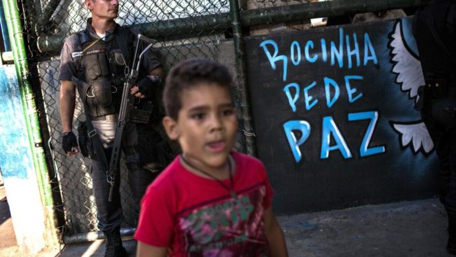 Uma criança passa enquanto um Policial militar vigia favela da Rocinha, no Rio de Janeiro, Brasil (26 de setembro de 2017). (FOTO: Mauro PIMENTEL/AFP)