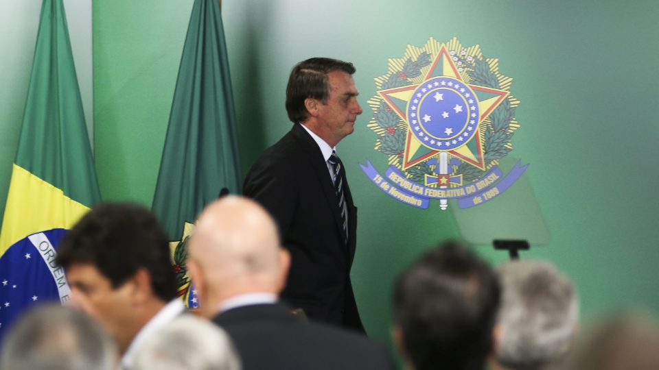 Bolsonaro caminha em solenidade no Palácio do Planalto em frente de um brasão da República.
