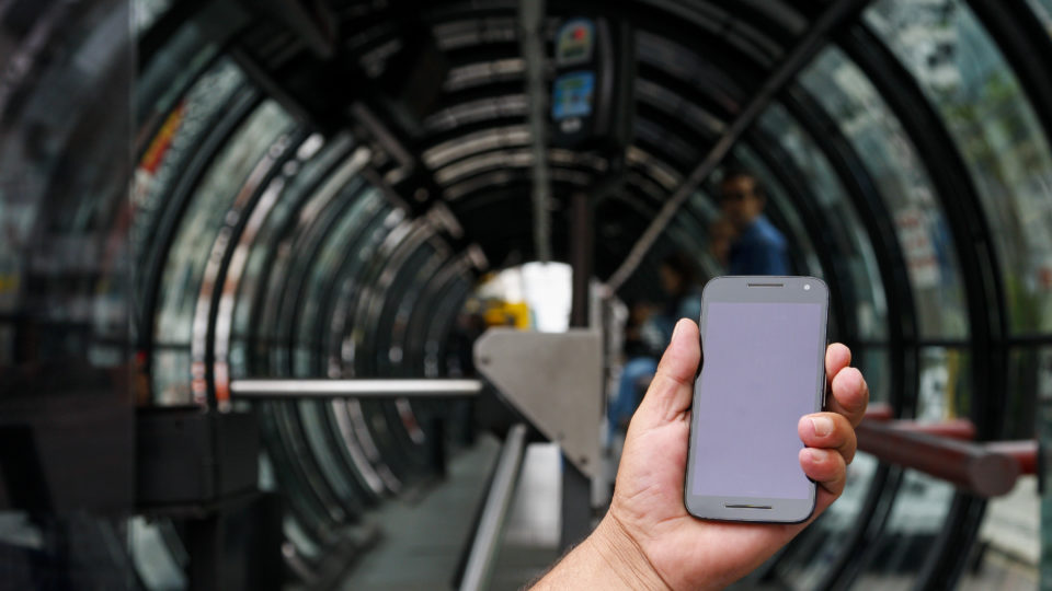 celular em uma mão em frente à estação-tubo em Curitiba