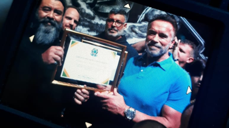 Alexandre Frota entrega certificado de reconhecimento ao ator Arnold Schwarzenegger enviado pelo presidente Jair Bolsonaro. O certificado diz: "Ao ilustríssimo senhor Arnold Schwarzenegger. Os agradecimentos da República Federativa do Brasil pela sua dedicação e integridade durante sua trajetória na vida artística, social e política"
