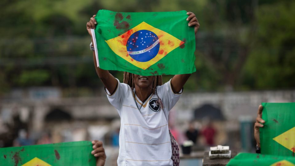 Manifestante ergue bandeira pintada de vermelho, simbolizando sangue, no enterro do músico Evaldo dos Santos Rosa.