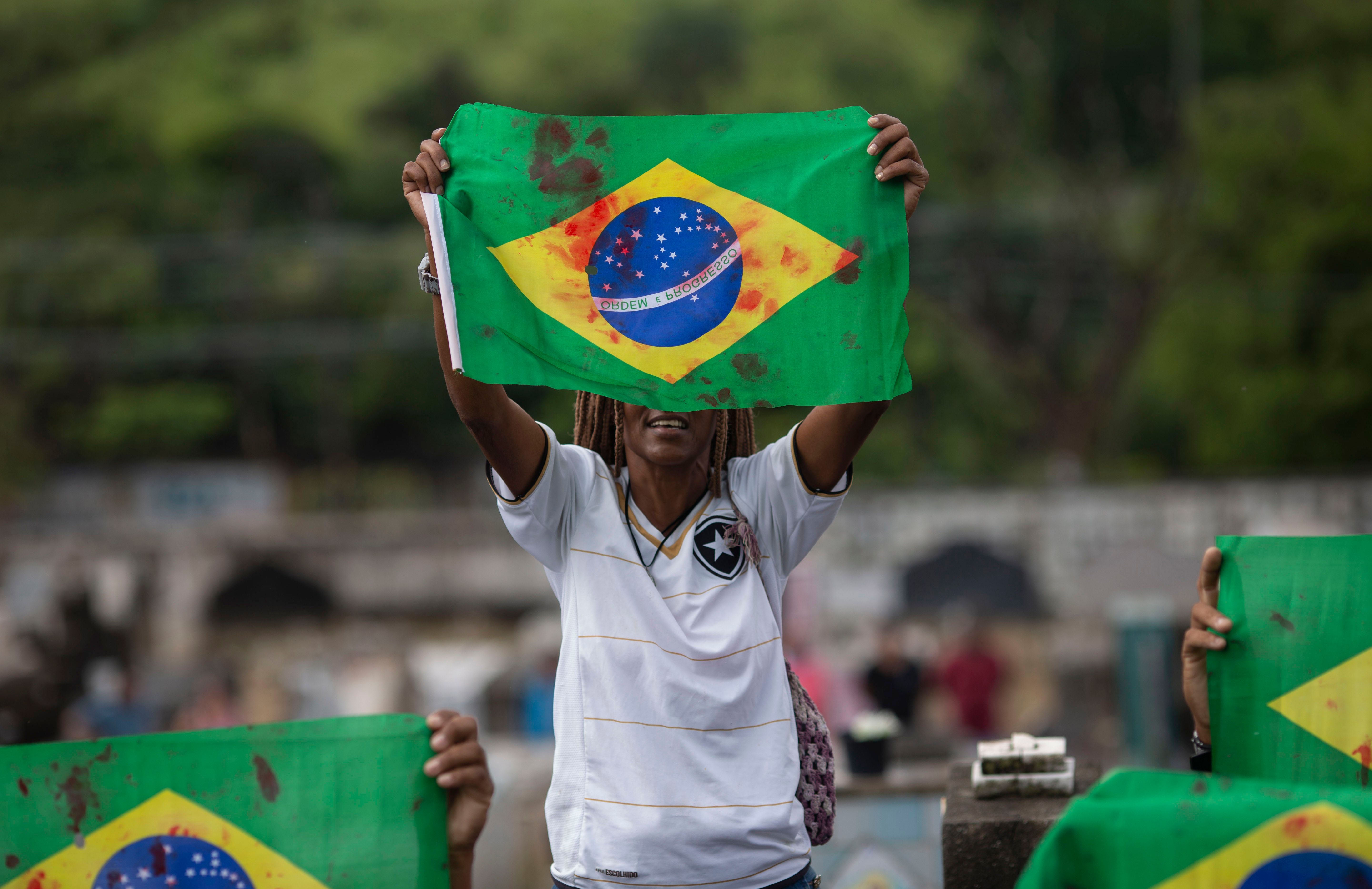 Manifestante ergue bandeira pintada de vermelho, simbolizando sangue, no enterro do músico Evaldo dos Santos Rosa.