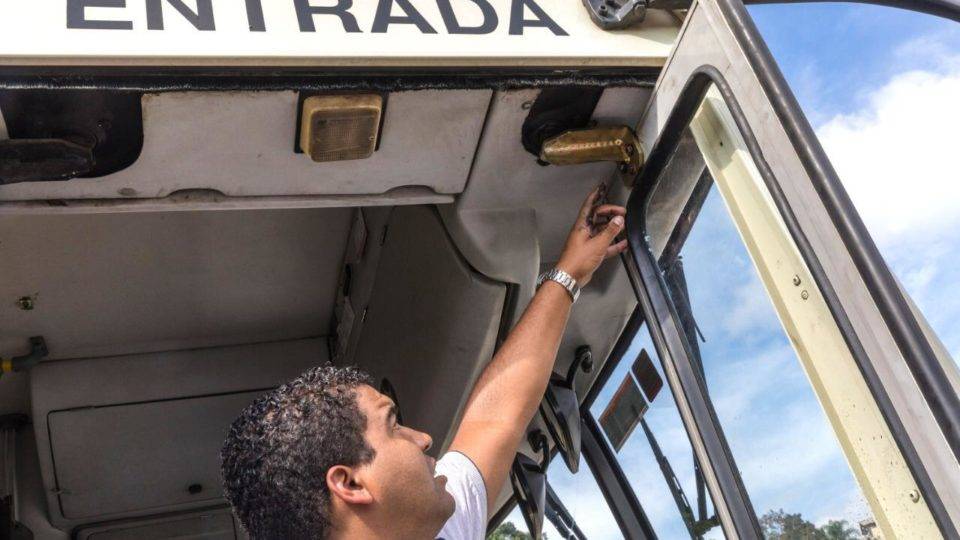 Homem mostra o suporte de sustentação da porta que estava danificado no ônibus.