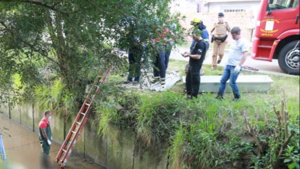 Policiais e bombeiros na beira do córrego