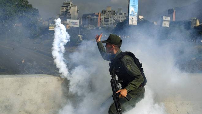 Membro da Guarda Nacional Bolivariana que agora apoia Juan Guaidó lança uma bomba de gás lacrimogêneo durante um confronto com guardas leais a Nicolás Maduro em frente à base militar de La Carlota em Caracas, em 30 de abril de 2019 | Foto: YURI CORTEZ / AFP
