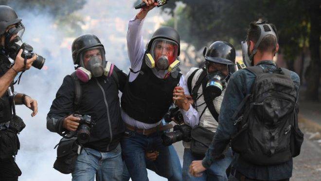 O jornalista venezuelano Gregory Jaimes (ao centro), do canal VPITV, é ajudado por colegas após ser ferido durante o confronto entre manifestantes e forças do regime de Maduro em Caracas, 1 de maio