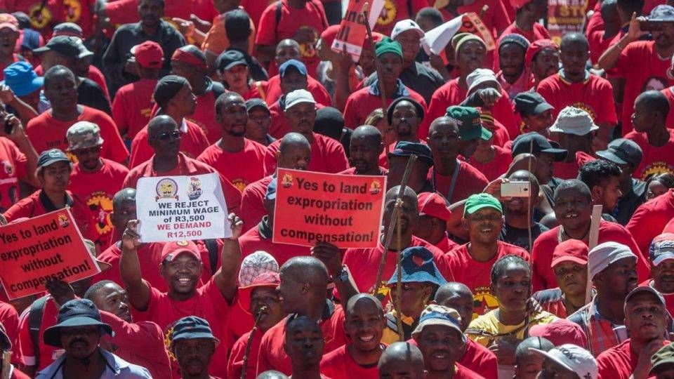 Membros da Federação Sul-Africana de Sindicatos, em marcha pela Cidade do Cabo durante greve geral, seguram cartaz onde se lê “sim para a expropriação de terras sem compensação”. | Mujahid Safodien/ AFP