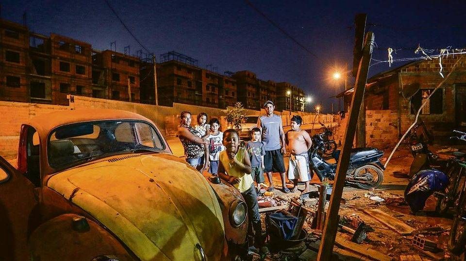 Verônica e Maicon com os quatro filhos e um vizinho, em uma área de invasão. Ao fundo, construção que vai receber funcionários da fábrica de Ortigueira. | Daniel Castellano/Gazeta do Povo