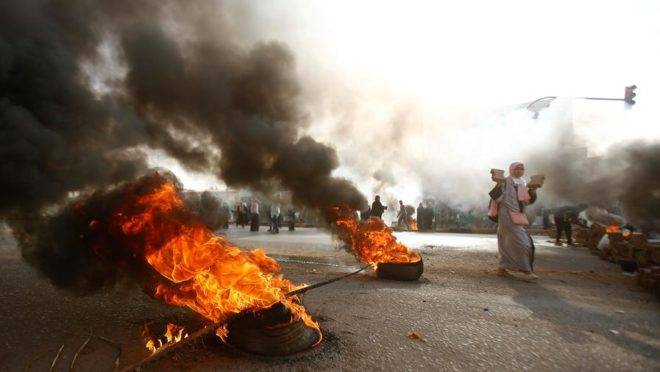 Manifestante sudanesa caminha perto de pneus em chamas enquanto forças militares tentam dispersar uma ocupação de manifestantes em frente à sede do Exército na capital, Cartum, 3 de junho