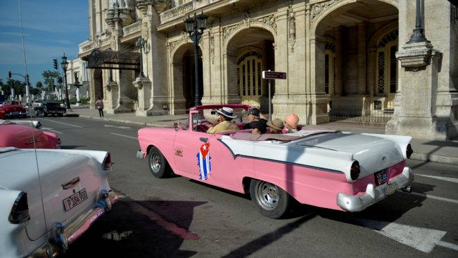 Taxista particular em um antigo carro americano leva os turistas nas ruas de Havana