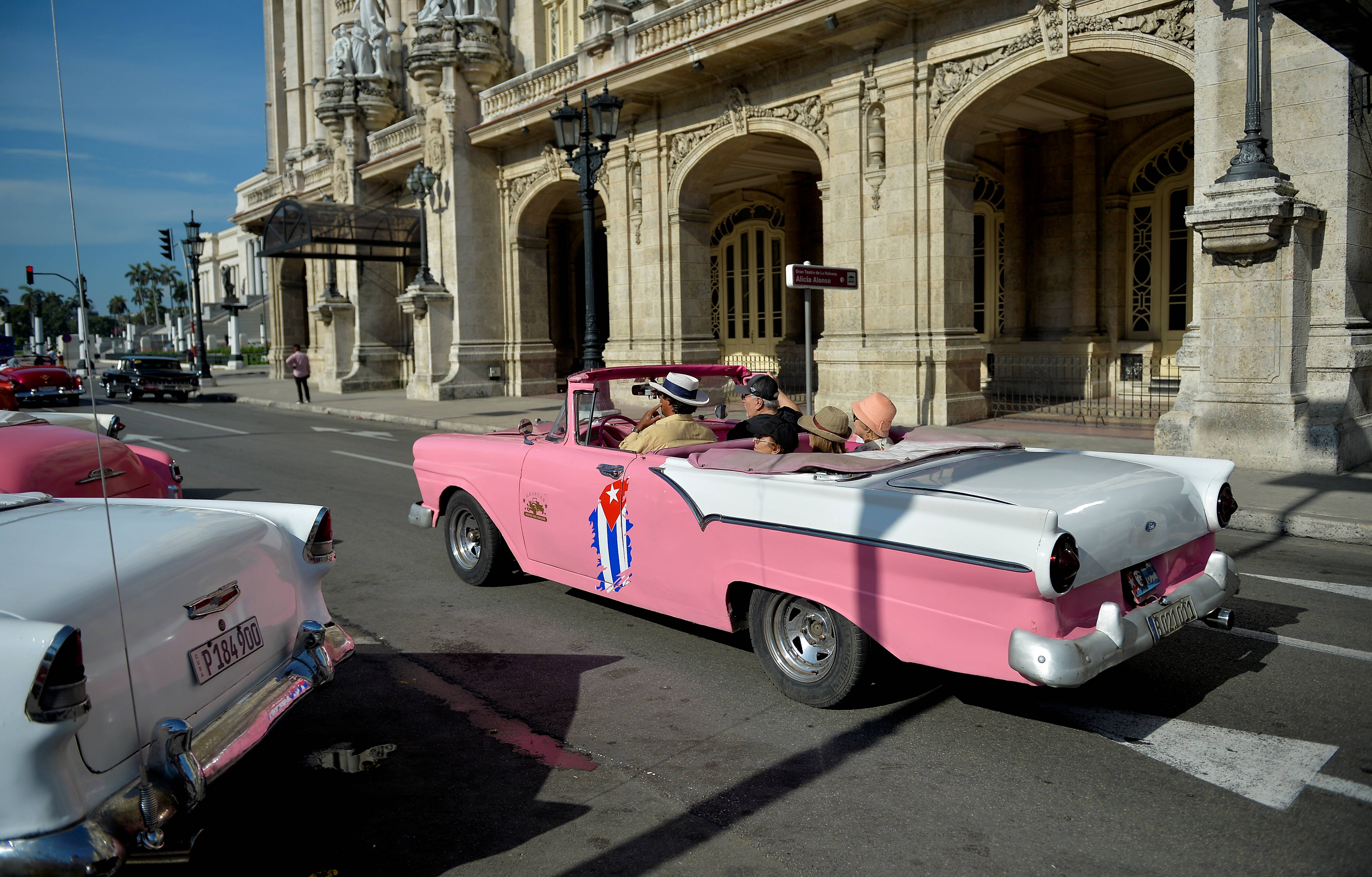 Taxista particular em um antigo carro americano leva os turistas nas ruas de Havana