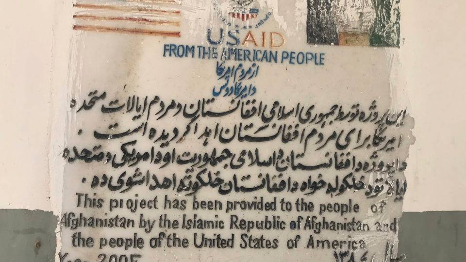 Uma placa com as bandeiras dos Estados Unidos e do Afeganistão e uma mensagem dizendo que a Agência dos EUA para Desenvolvimento Internacional ajudou a construir a escola em 2015, no interior da escola para meninas Sher Ali Khan em Naw Deh, na província de Farah, Afeganistão, em abril de 2019