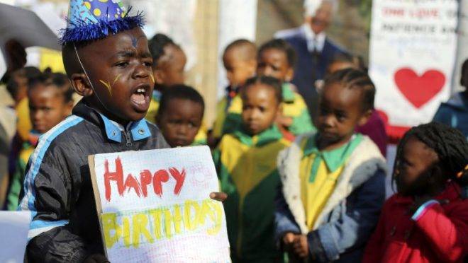 Menino canta segurando um cartaz em que deseja feliz aniversário a Madiba, nome do clã de Mandela |