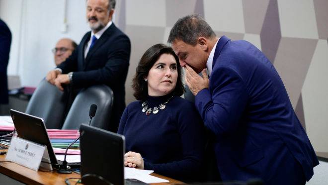 O senador Marcio Bittar, relator do projeto de Moro, cochicha no ouvido da presidente da CCJ, Simone Tebet.