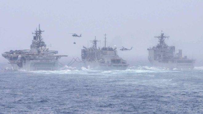 O navio anfíbio de assalto USS Boxer, à esquerda, e o USS Harpers Ferry, à direita, conduzem um reabastecimento no mar com o navio de apoio de combate rápido USNS Arctic. Eles estão posicionados na área de operação da 5a Frota dos EUA