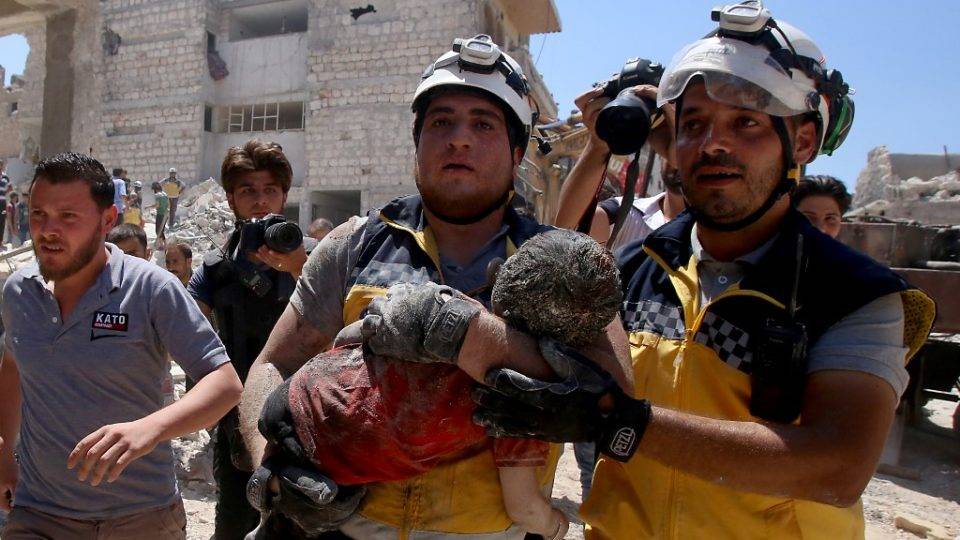 Membros da defesa civil da Síria, conhecidos como capacetes brancos, retiram uma criança com vida, mas ferida, dos escombros após um ataque aéreo atribuído à Rússia em Maaret al-Numan, na província de Idlib, em 22 de julho de 2019