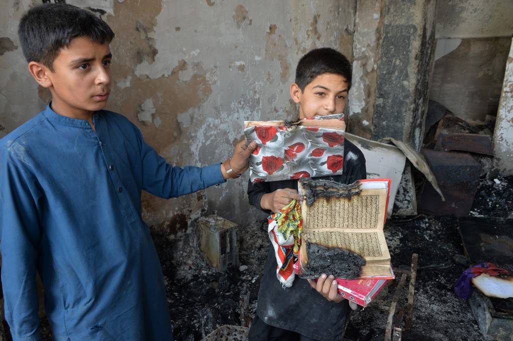 Crianças afegãs mostram os restos queimados de um exemplar do Alcorão perto do local de um ataque em Cabul, em 29 de julho de 2019, um dia após um ataque letal contra um comitê de campanha eleitoral. A violência marcou o início do período de eleições no Afeganistão no fim de semana