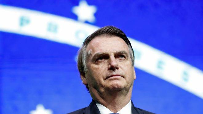 Bolsonaro na frente da bandeira do Brasil.