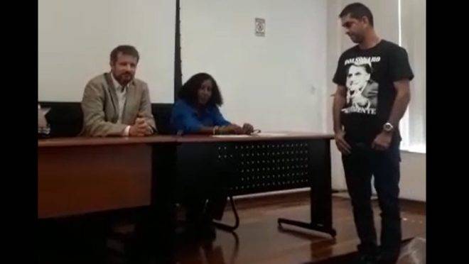 Imagem de vídeo que mostra o coordenador do curso de Segurança Pública da UFF tentando impedir um aluno com uma camiseta pró-Bolsonaro de fazer o juramento em sua formatura.
