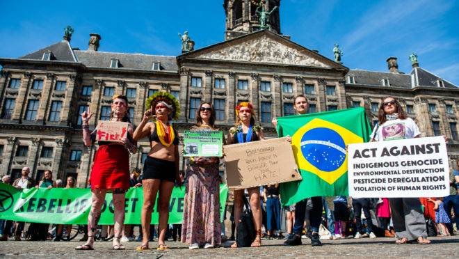 Manifestantes seguram cartazes contra políticas ambientais do governo brasileiro em Amsterdã, Holanda