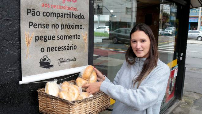 Luiza Adriano da Tradicionale Café & Panificadora que põe uma cesta com pães e salgados para doação do lado de fora do estabelecimento.