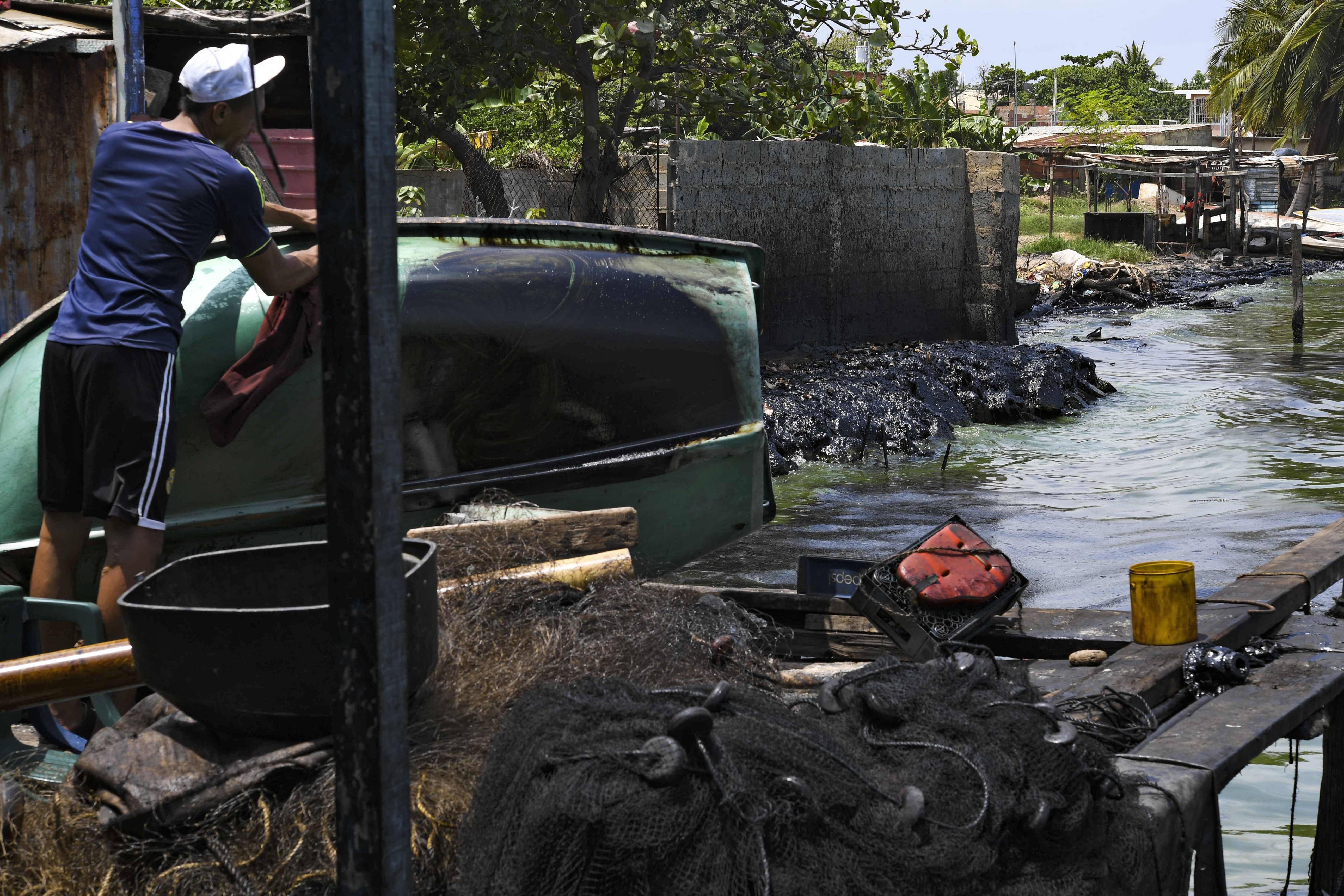 Um pescador limpa o óleo de seu barco, nas margens do poluído lago Maracaibo | Foto: YURI CORTEZ / AFP Um pescador limpa o óleo de seu barco, nas margens do poluído lago Maracaibo | Foto: YURI CORTEZ / AFP