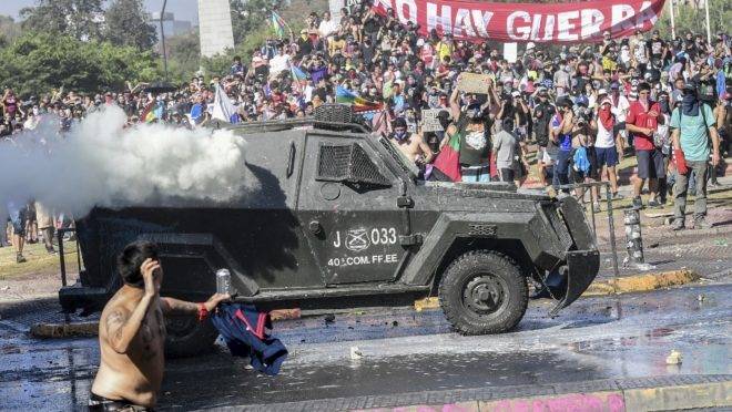 Manifestante atira pedra em veículo da polícia durante protestos em Santiago, Chile, 24 de outubro de 2019