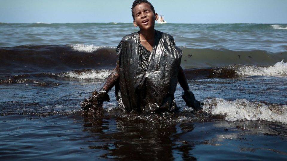 Petrobras identifica origem de óleo que contamina o litoral do Nordeste Garoto caminha por mancha de óleo em praia de Pernambuco: riscos à saúde.
