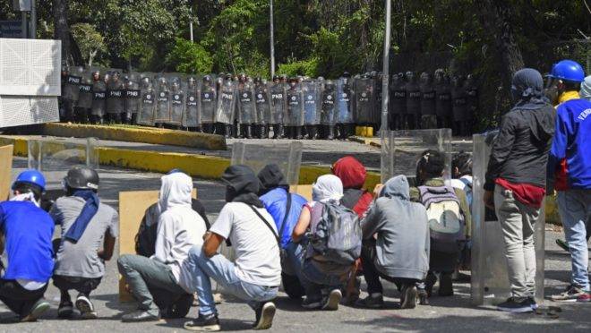 Estudantes universitários se protegem durante enfrentamento com a Polícia e a Guarda Bolivariana na entrada da Universidad Central de Venezuela, em Caracas, 14 de novembro de 2019