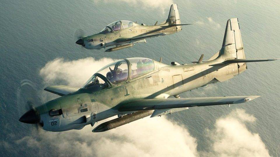 Dois aviões militares do modelo Super Tucano da Embraer sobrevoam o mar.